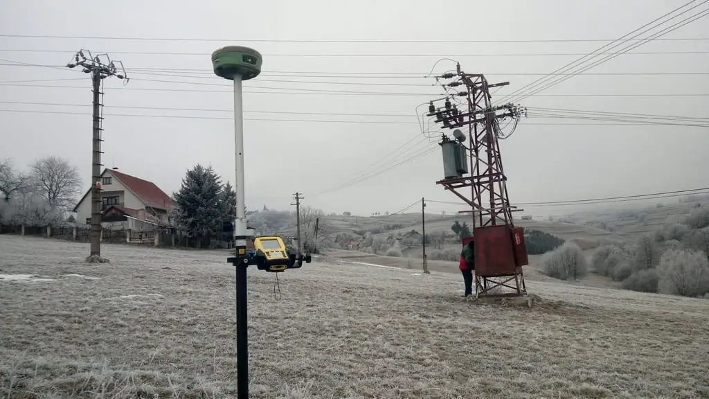 GNSS prijímač na výtyčke na zamrznutej lúke pri stĺpe elektrického vedenia