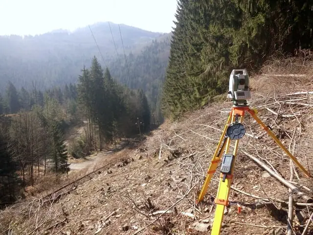 Totálna stanica na strmom svahu vo výrube nad dolinou s elektrickým vedením