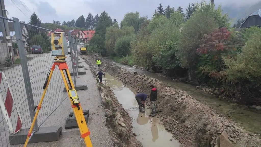 Totálna stanica pri výkope pozdĺž potoka a cesty