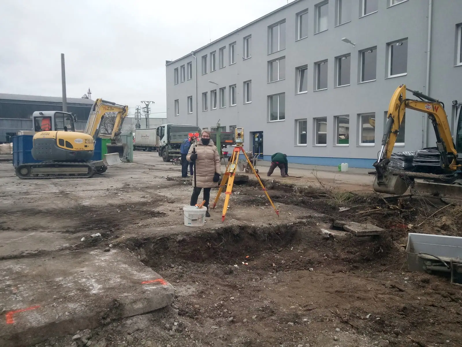 Totálna stanica na stavenisku s bagrami pred administratívnou budovou
